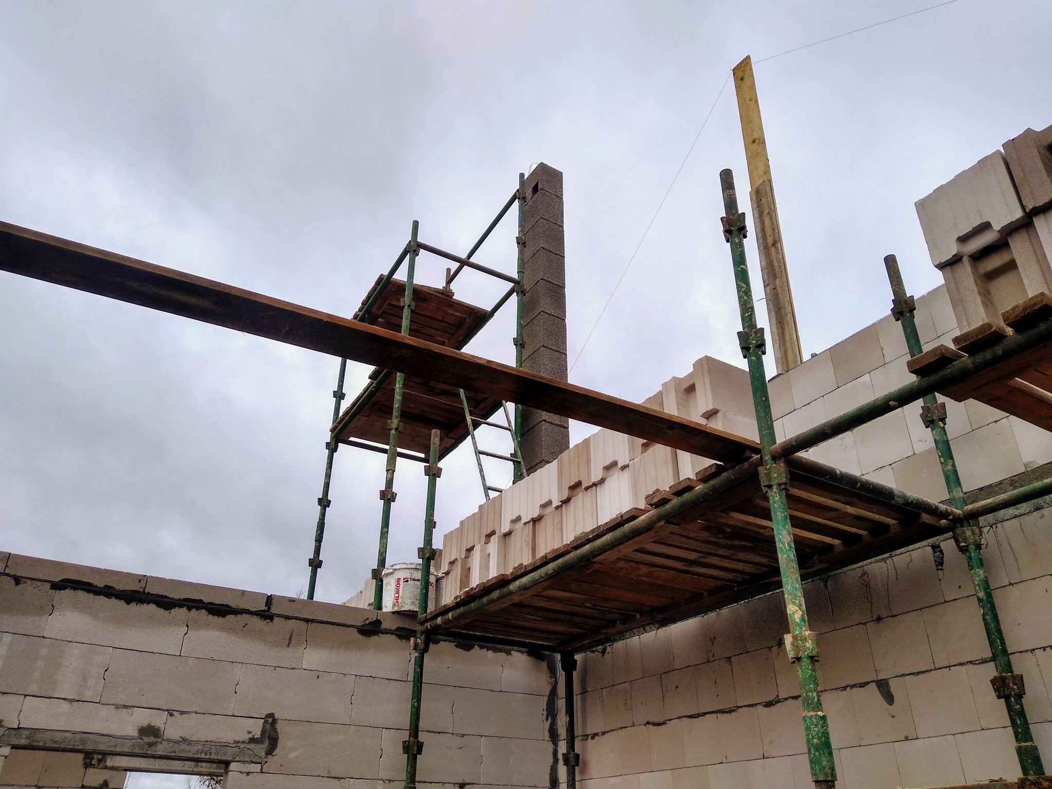 Wznoszenie ściany z bloczków betonu komórkowego Ytong na rusztowaniu, widoczny komin z pustaków wentylacyjnych, pojemnik z zaprawą murarską na podeście.