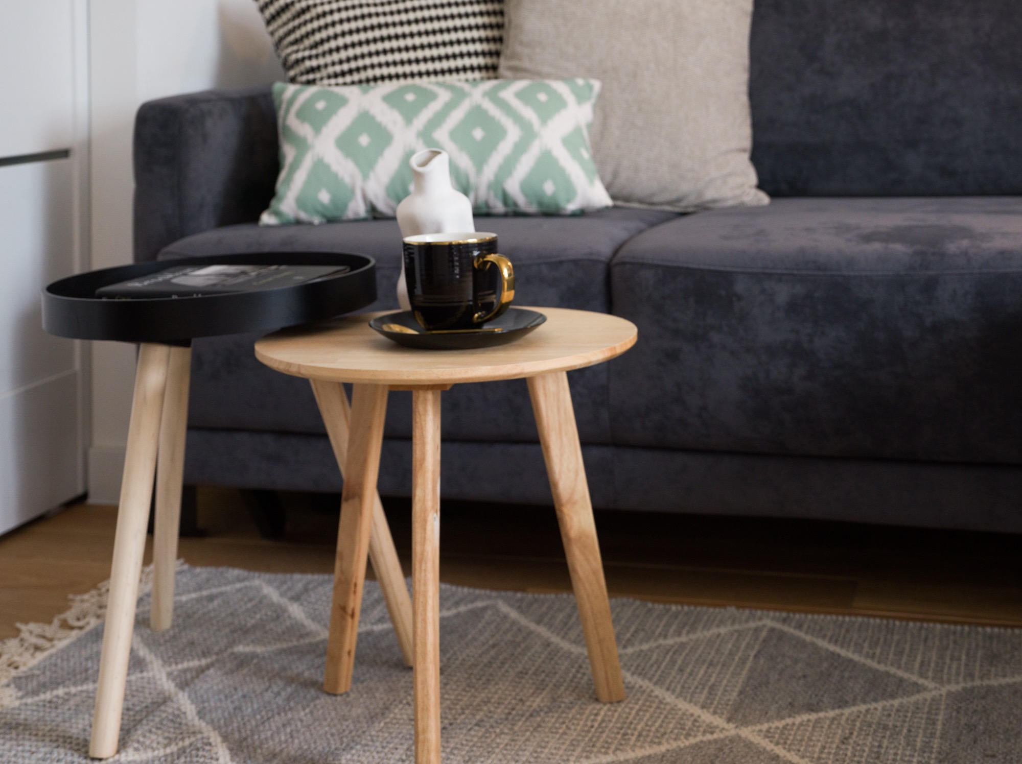 Stylowy kącik kawowy: czarna filiżanka na drewnianym stoliku, szara sofa z dekoracyjnymi poduszkami, dywan w geometryczne wzory. Przytulna aranżacja wnętrza.