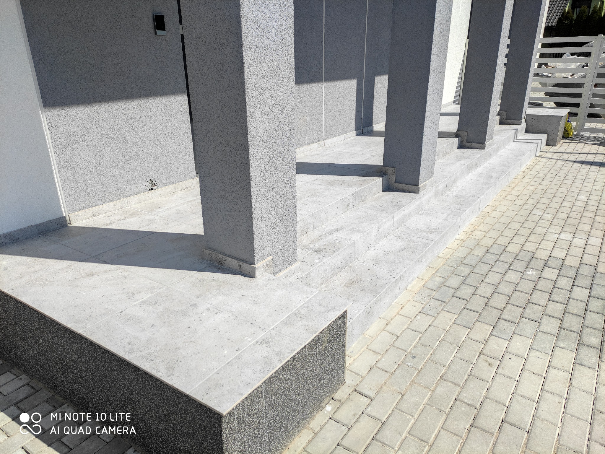 Wykończone schody wejściowe z szarymi płytkami i kolumnami, prowadzące do drzwi wejściowych, z kostką brukową na podjeździe.