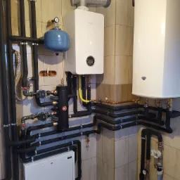 Zrealizowana instalacja centralnego ogrzewania z piecem gazowym Bosch, zbiornikiem buforowym i zasobnikiem wody, rury w izolacji, płytki ceramiczne na ścianach.