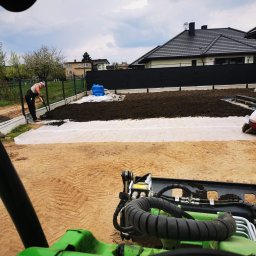 Xenimar - Przygotowanie terenu pod trawnik: wyrównywanie ziemi na geowłókninie, widok z kabiny miniładowarki, w tle ogrodzenie panelowe i dom