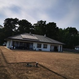 Xenimar - Przygotowany teren pod trawnik z rolki przed nowoczesnym domem jednorodzinnym; widoczne ślady po pracy maszyn, czarna obrzeża i zainstalowane lampy ogrodowe