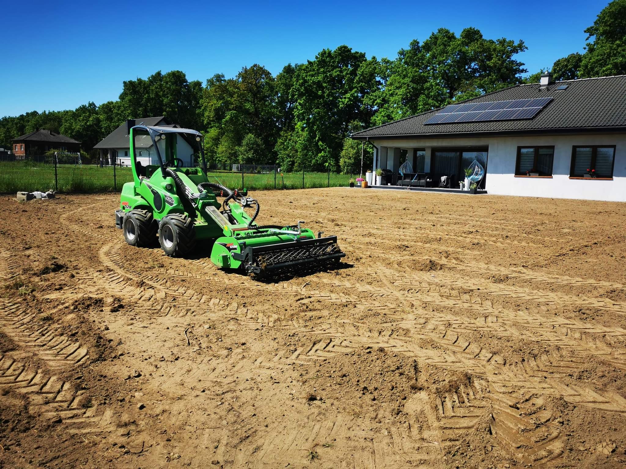 Przygotowanie terenu pod trawnik z wykorzystaniem glebogryzarki separacyjnej Avant 528, widoczne ślady opon na wyrównanej ziemi, w tle dom z panelami słonecznymi i ogrodzenie.