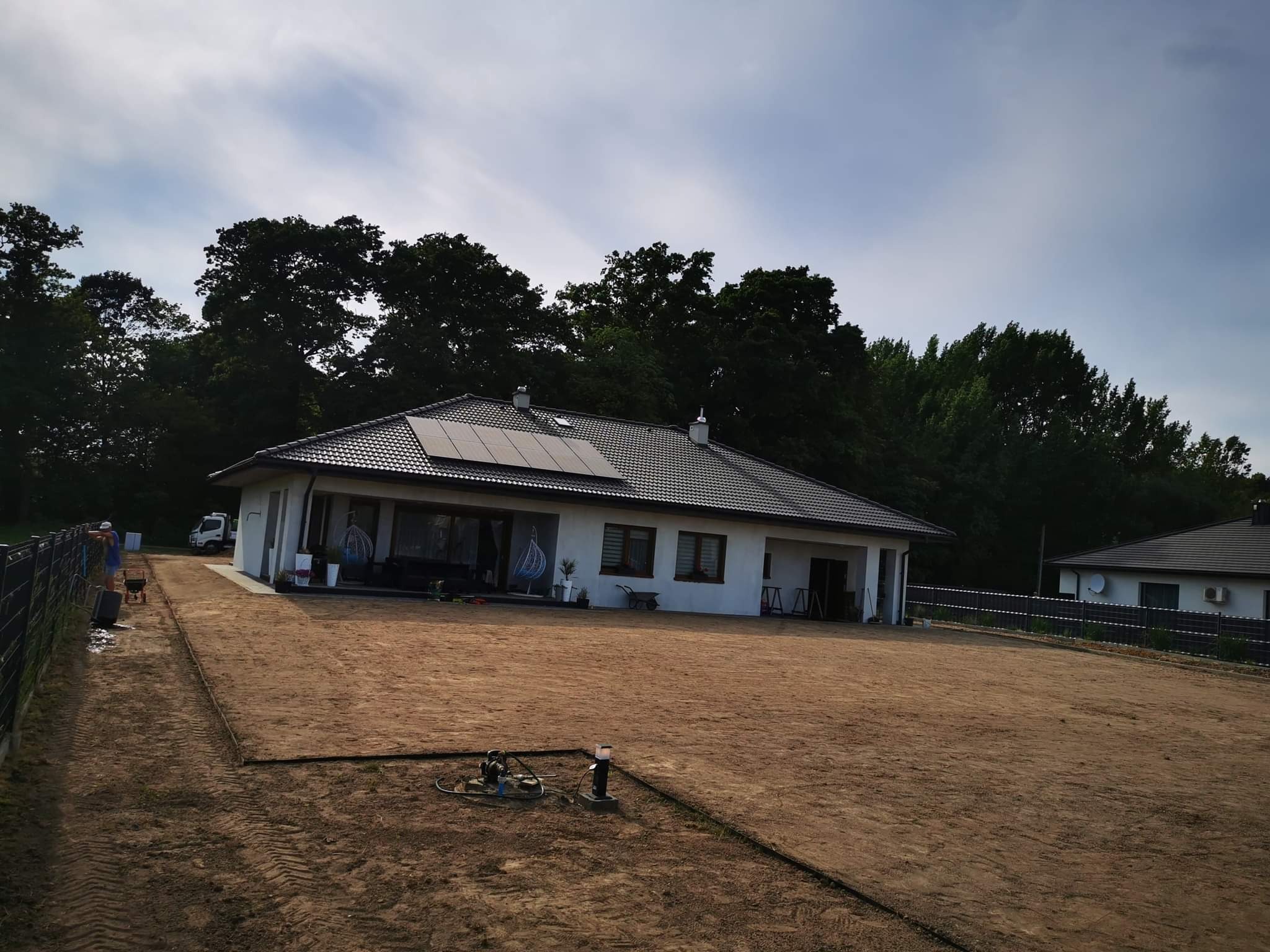 Przygotowany teren pod trawnik z rolki przed nowoczesnym domem jednorodzinnym; widoczne ślady po pracy maszyn, czarna obrzeża i zainstalowane lampy ogrodowe