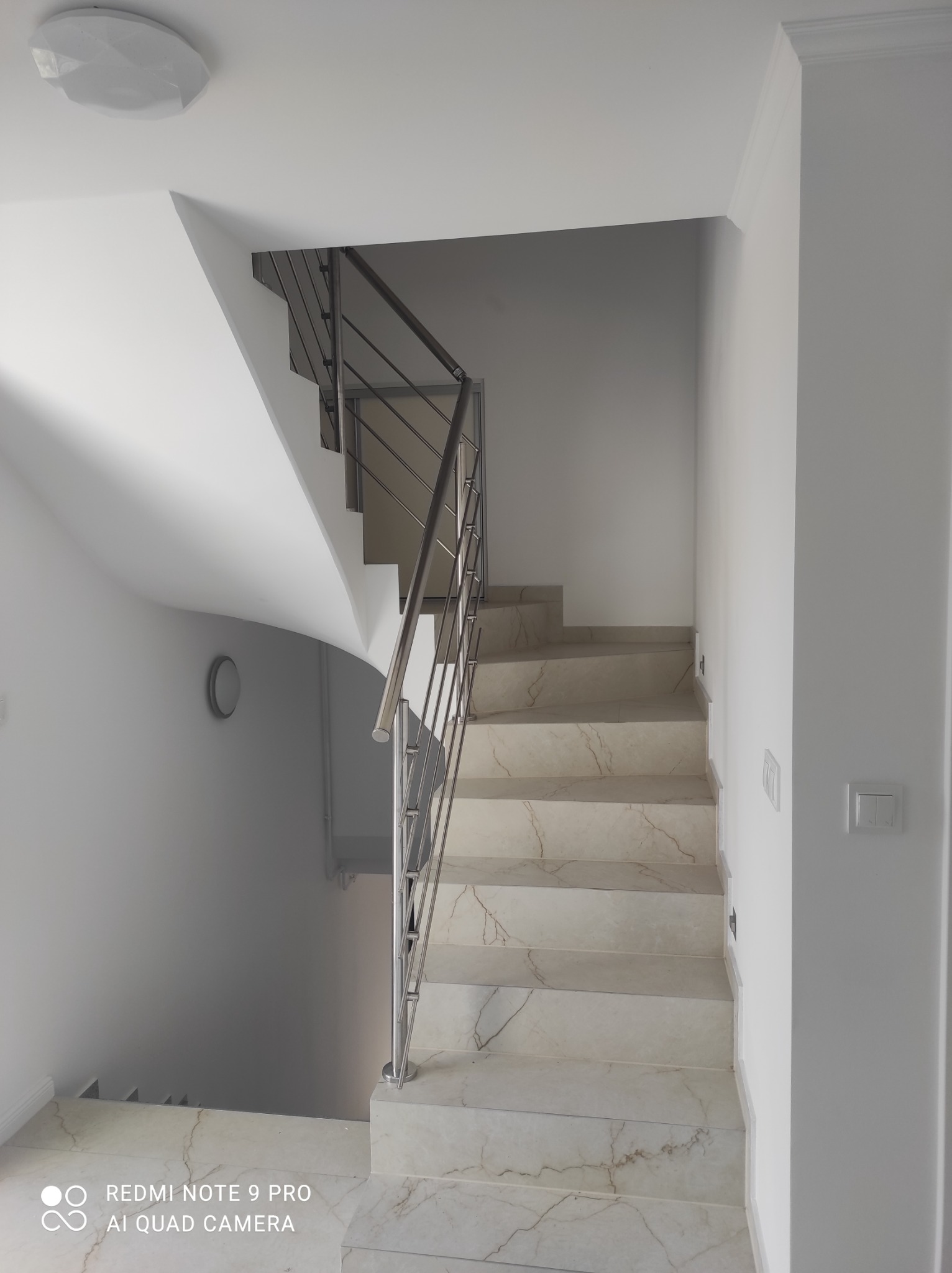 Schody wewnętrzne wyłożone marmurem z metalową balustradą w nowoczesnym, jasnym wnętrzu.