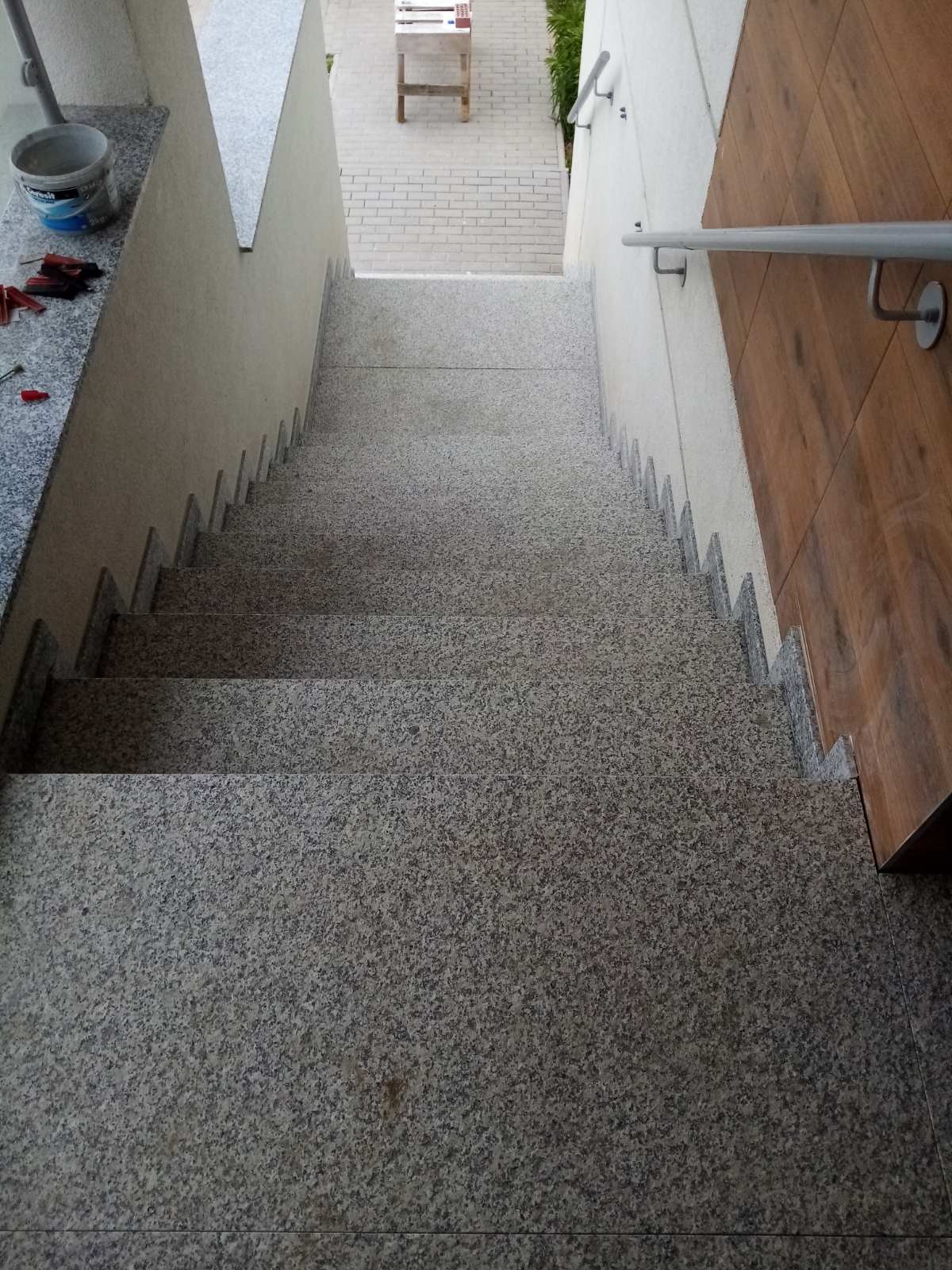 Granitowe schody zewnętrzne z drewnianą okładziną ściany po prawej stronie, widok z góry na dół, z widocznym wiadrem i narzędziami na górnym podeście.