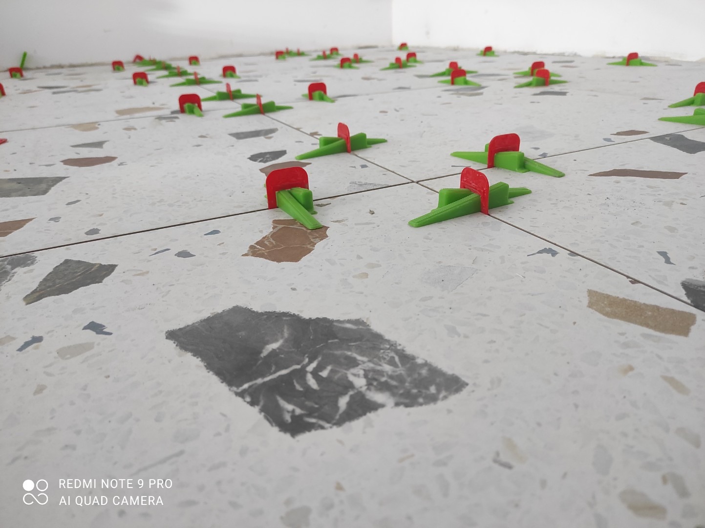 Ułożona podłoga z płytek lastryko z użyciem zielonych i czerwonych klipsów poziomujących, widok z niskiej perspektywy.