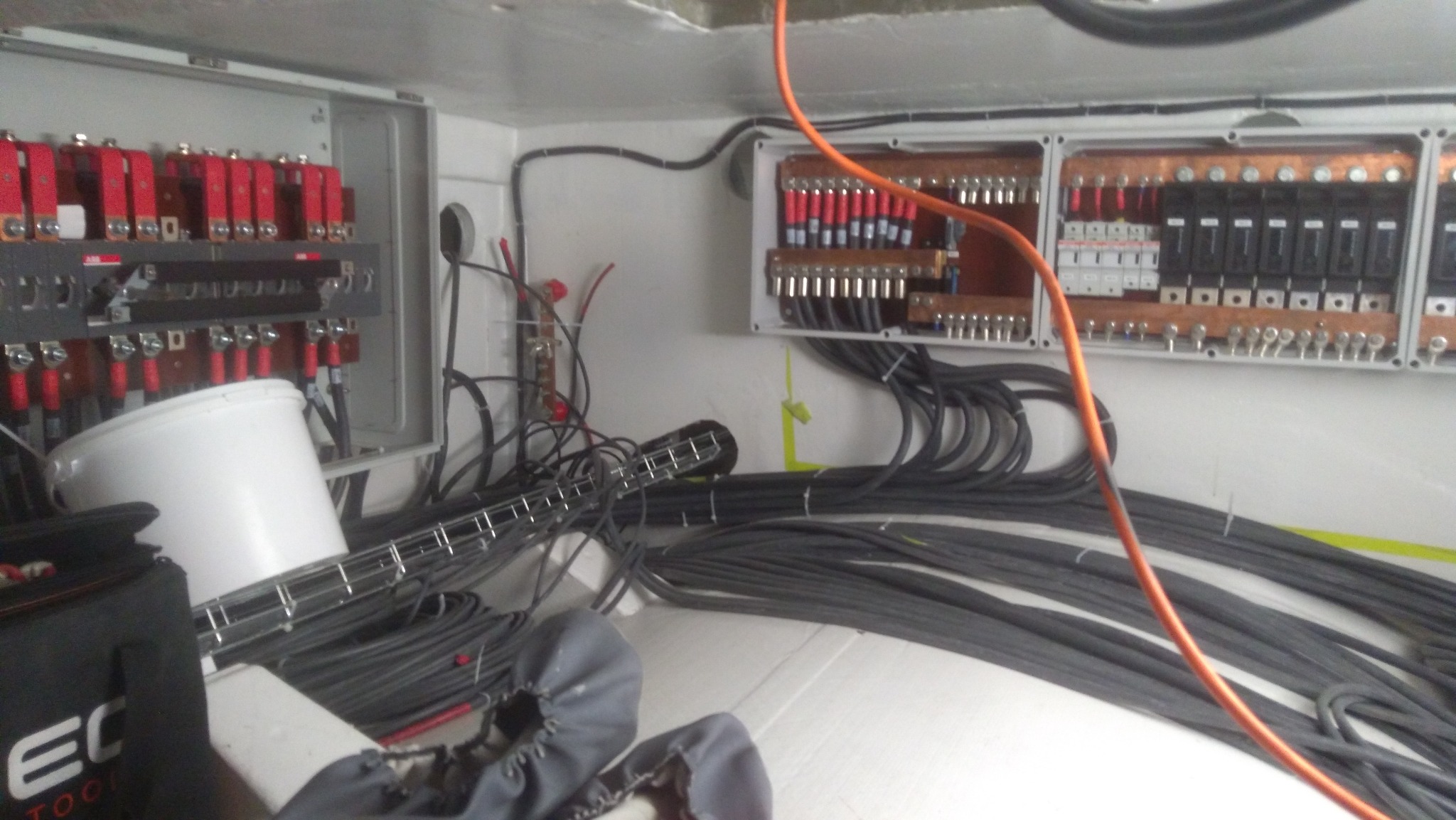 Rozdzielnice elektryczne z licznymi przewodami, część z nich ułożona w wiązki, widoczny także biały pojemnik i torba narzędziowa.