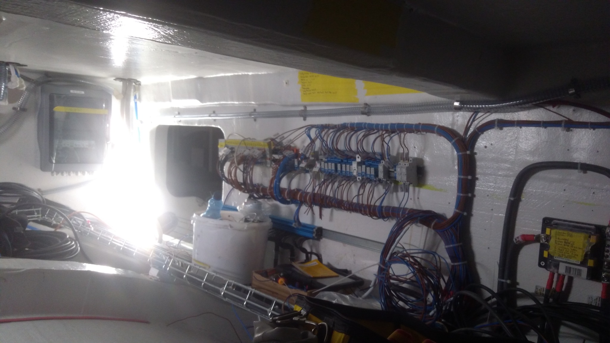 Rozbudowana instalacja elektryczna w trakcie montażu wewnątrz pomieszczenia, widoczne kable, skrzynka rozdzielcza, narzędzia i elementy mocujące.