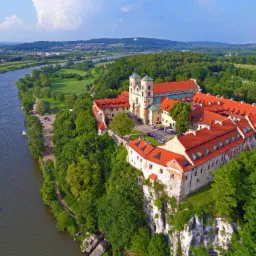 Klasztor w Tyńcu, widok z lotu ptaka na budynek z czerwonym dachem, położony na skale nad Wisłą, z widoczną panoramą okolicy.