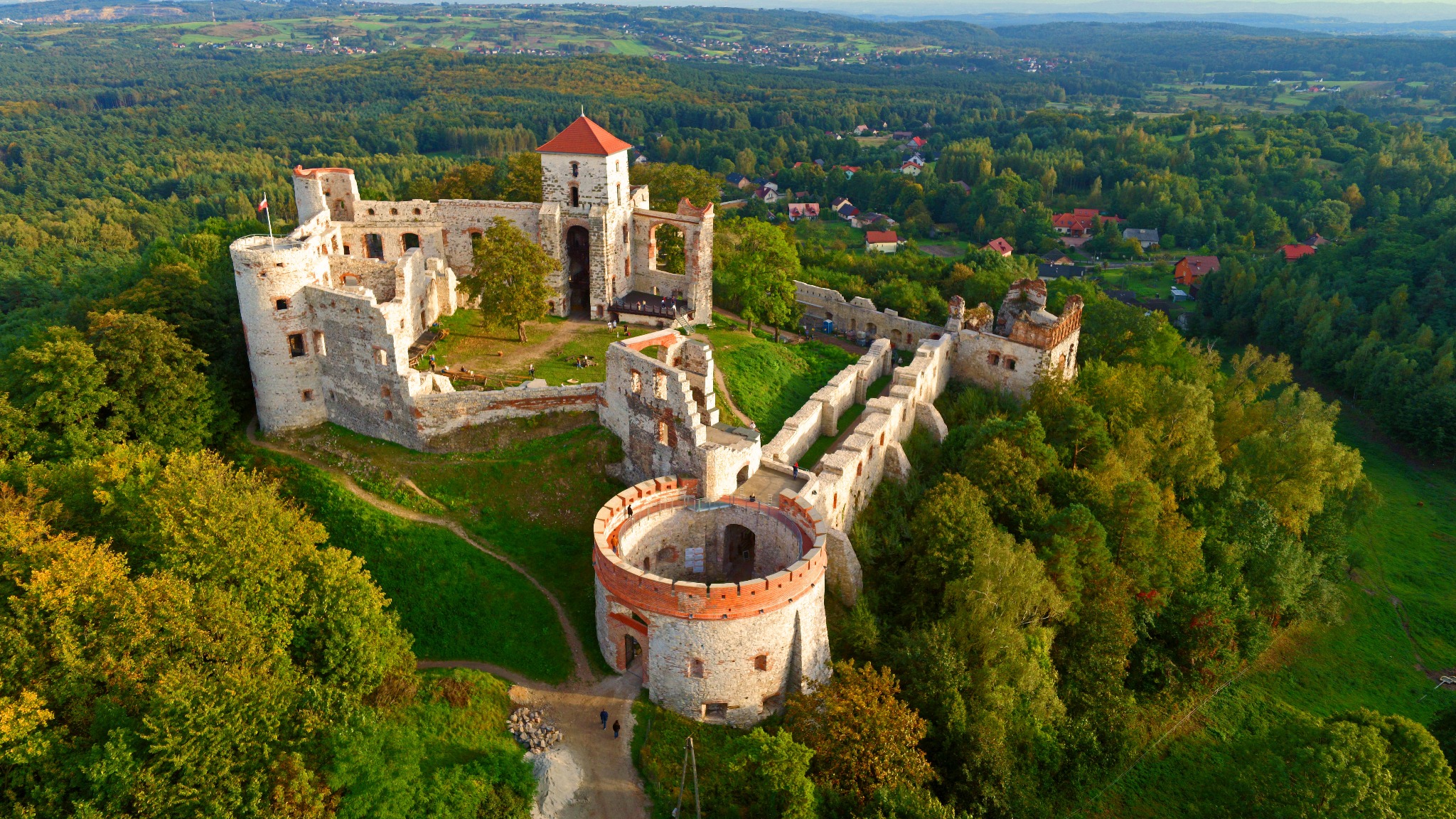 Panorama z lotu ptaka na ruiny średniowiecznego zamku w otoczeniu lasów i wzgórz.