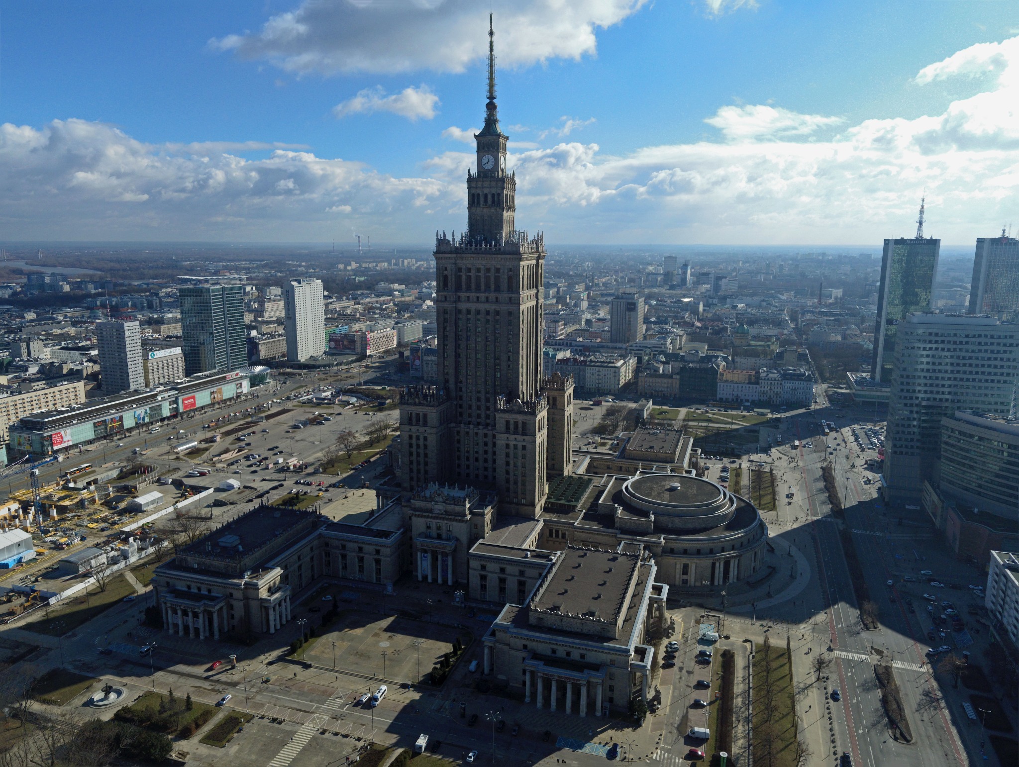 Panorama Warszawy z Pałacem Kultury i Nauki w centrum, uchwycona z lotu ptaka w słoneczny dzień z chmurami.