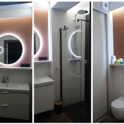 Nowoczesna łazienka po remoncie: okrągłe lustro z podświetleniem LED, kabina prysznicowa z czarnymi elementami i biała umywalka z szafką. Oświetlenie górne.