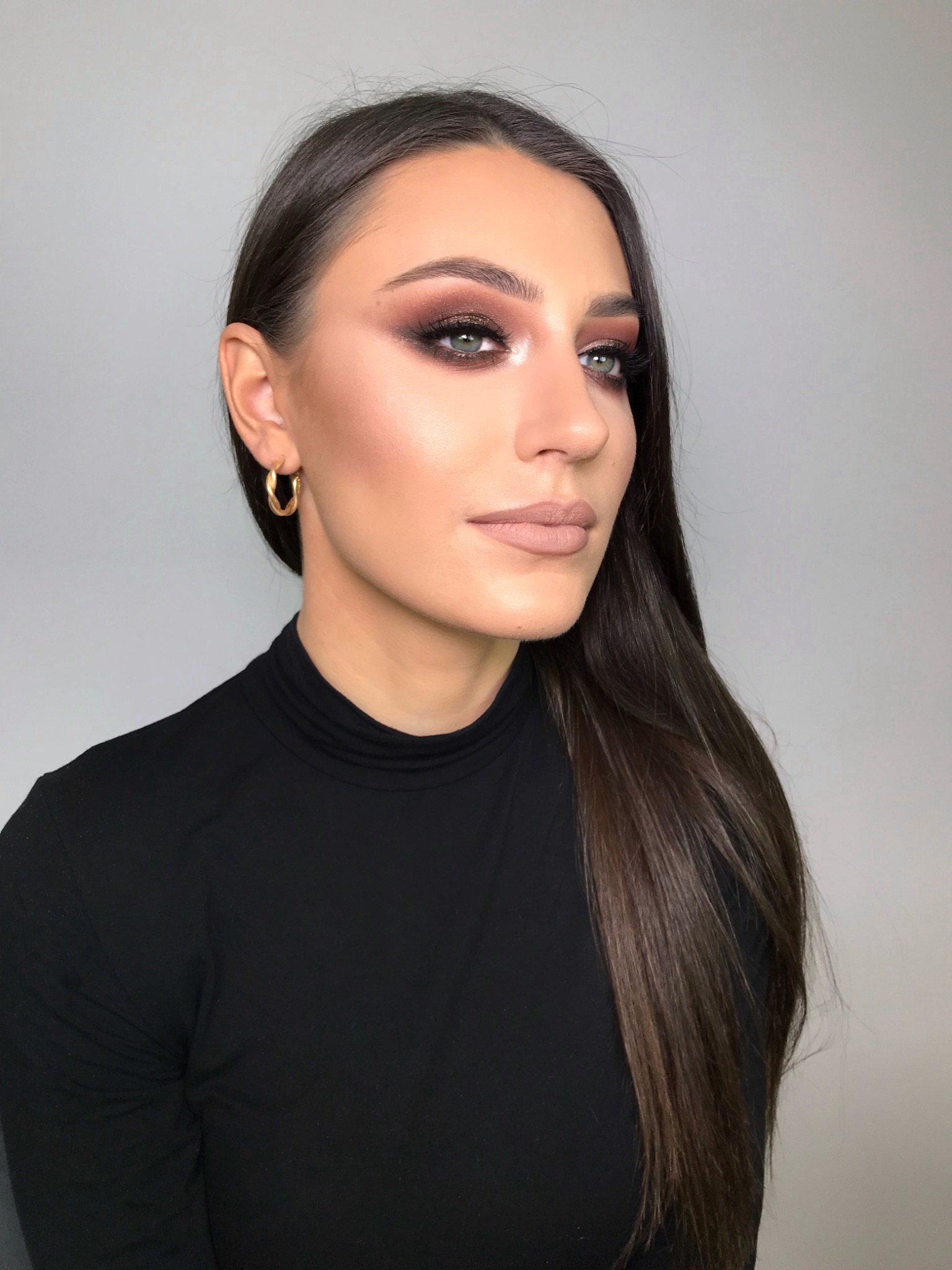 Portret kobiety z profesjonalnym, wieczorowym makijażem: intensywne, brązowe cienie na powiekach z połyskującymi drobinkami, precyzyjny kontur ust w odcieniu nude, delikatne podkreślenie kości...