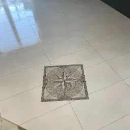 Błyszcząca, kremowa podłoga z płytek ceramicznych z dekoracyjnym, centralnym wzorem wiatrowej róży w odcieniach szarości i beżu.