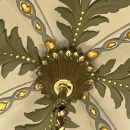 GBK - Detal bogato zdobionego sufitu z motywami roślinnymi i dekoracyjnym żyrandolem z łańcuchem, widok z dołu.