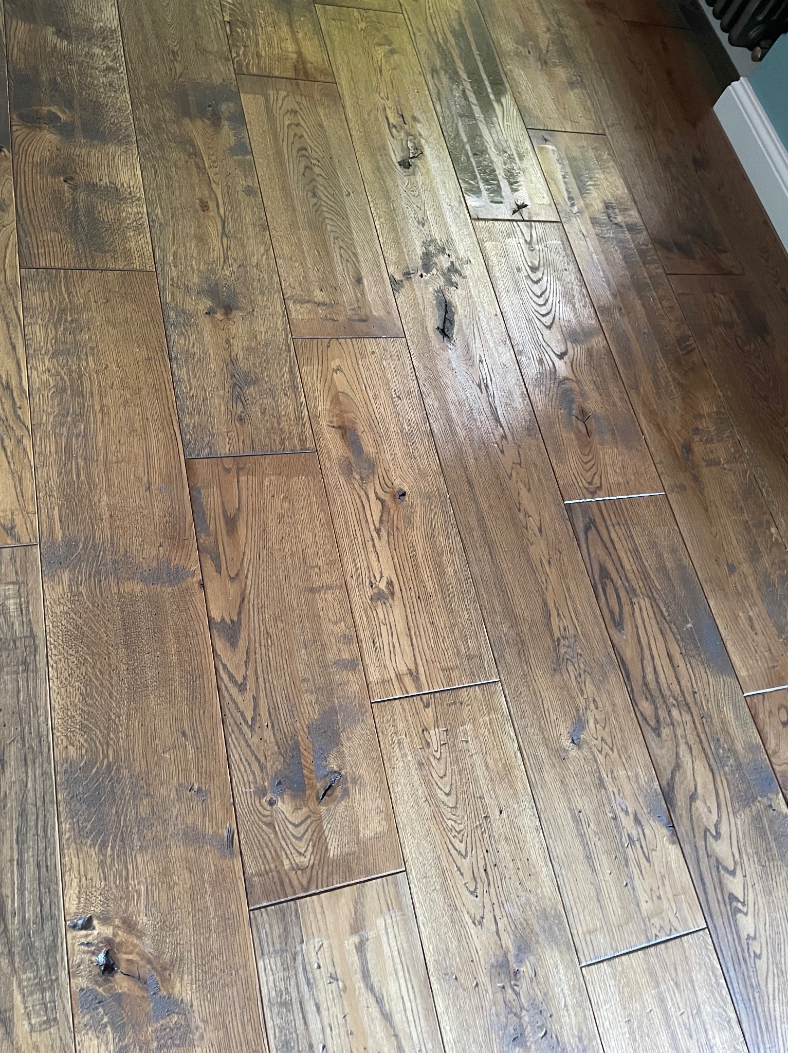 Ułożona, lakierowana podłoga z desek z widocznymi sękami i naturalnym usłojeniem, z fragmentem grzejnika i listwy przypodłogowej w tle.