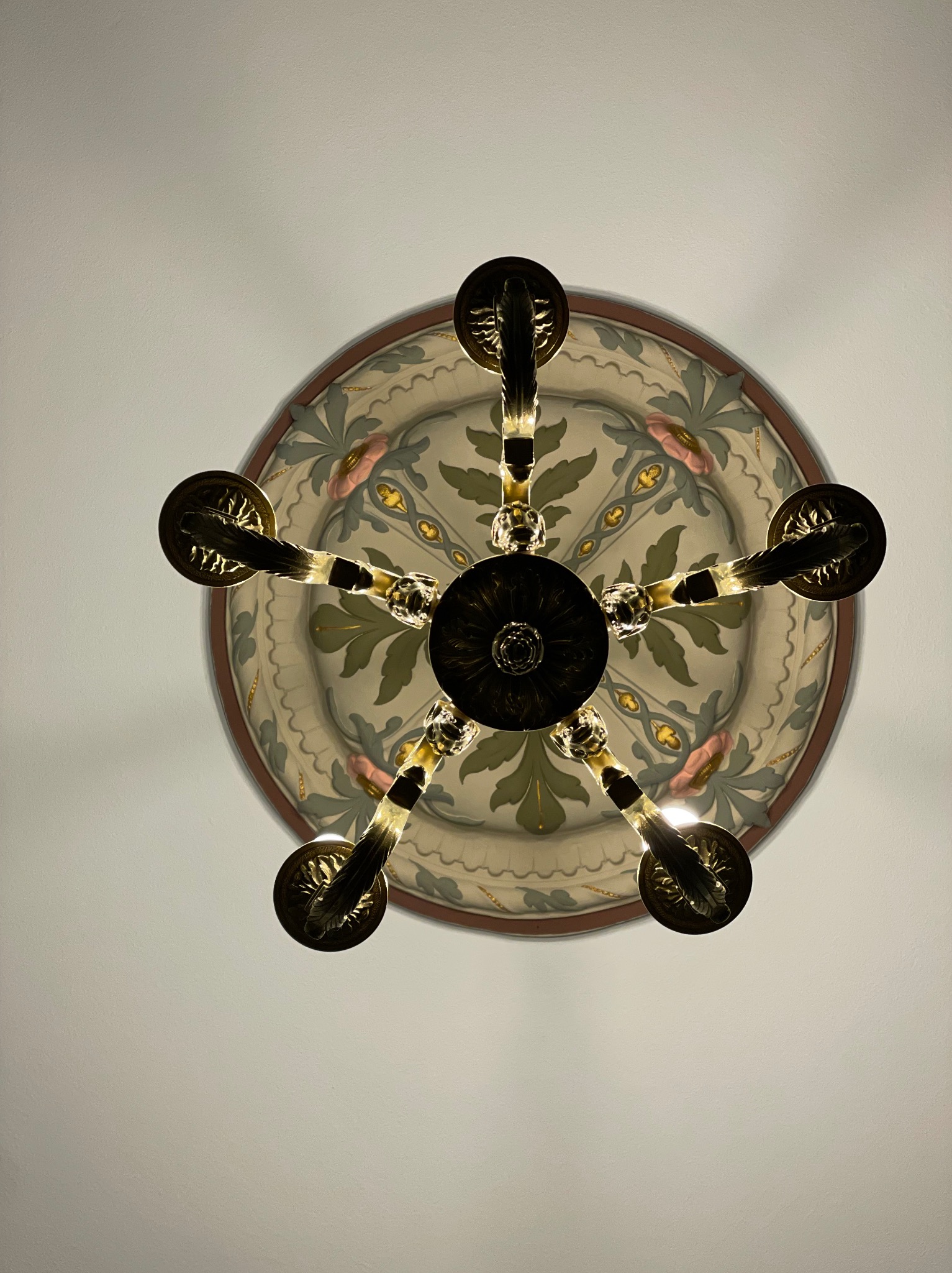 Widok z dołu na ozdobny sufit z malowidłami florystycznymi i żyrandol z pięcioma ramionami w stylu retro, z ciepłym światłem.