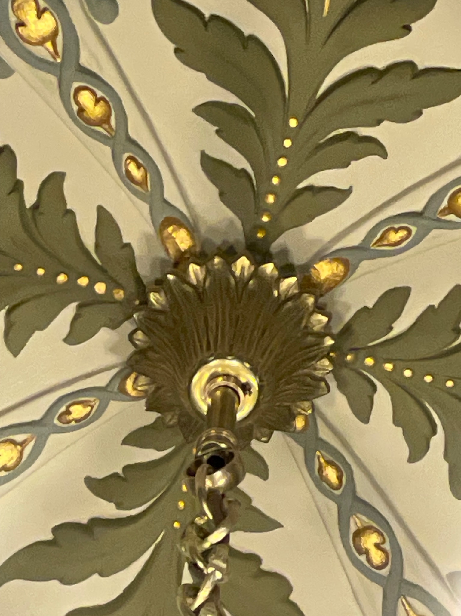 Detal bogato zdobionego sufitu z motywami roślinnymi i dekoracyjnym żyrandolem z łańcuchem, widok z dołu.