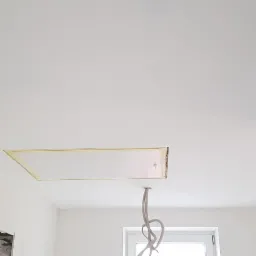 Biały sufit z otworem i widocznymi przewodami elektrycznymi, świeżo pomalowane ściany i fragment okna w tle.