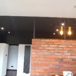 Nowoczesne wnętrze z ceglaną ścianą, czarnym sufitem z oświetleniem punktowym, designerską lampą wiszącą i grzejnikiem panelowym.