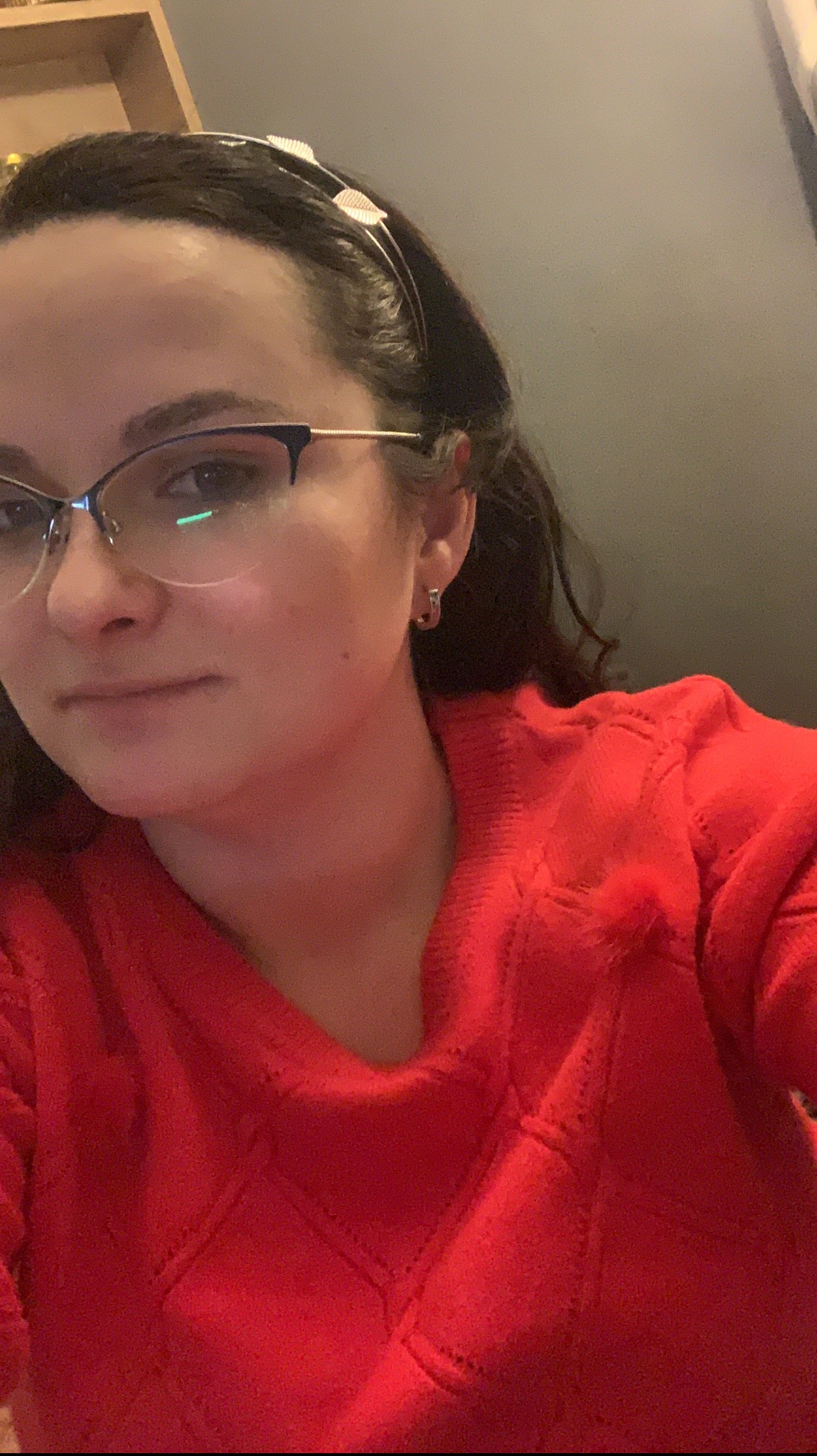 Portret kobiety w okularach i czerwonym swetrze z wzorem rombów, z opaską z motywem liści na włosach, ujęcie z bliska.