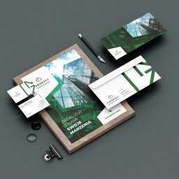 Wojoweb- Nowoczesne strony internetowe - Zestaw materiałów firmowych z logo firmy Zagórscy Nieruchomości: wizytówki, ulotka w ramce, koperta i karta pocztowa, ułożone na szarym tle z dodatkami biurowymi.