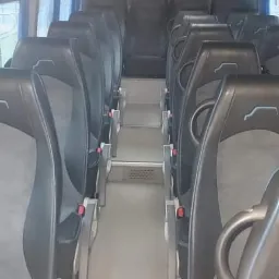 Wnętrze autobusu z rzędami czarnych foteli z szarymi wstawkami, widok na przejście z metalowymi stopniami.