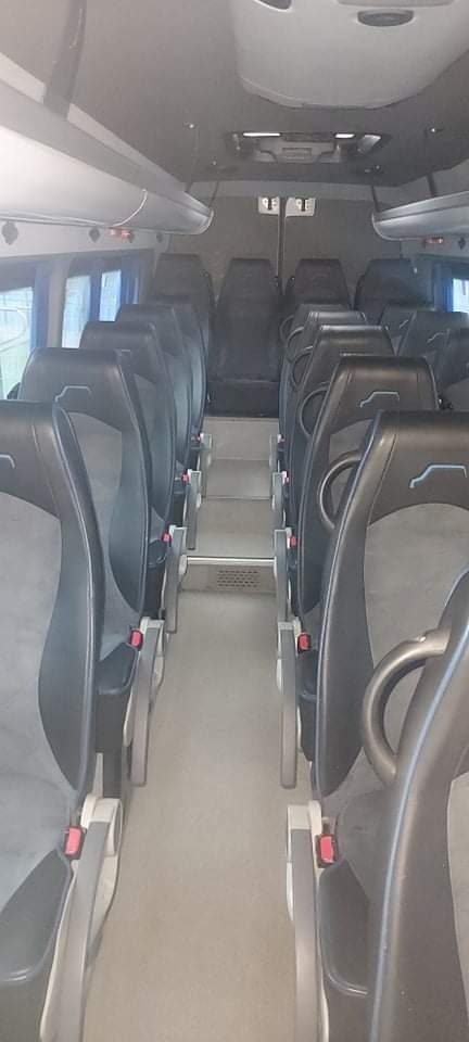 Wnętrze autobusu z rzędami czarnych foteli z szarymi wstawkami, widok na przejście z metalowymi stopniami.