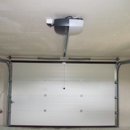 Phtu Control - Zamknięta biała brama garażowa segmentowa z napędem Nice Spin zamontowanym pod sufitem garażu, widoczna drabina aluminiowa z boku.