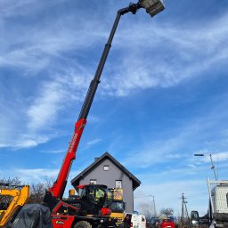 LITBUD Mateusz Litewka - Czerwono-czarny podnośnik teleskopowy Manitou z wysuniętym ramieniem i platformą roboczą na tle błękitnego nieba z chmurami, zaparkowany na żwirowym placu budowy z widocznymi innymi maszynami...