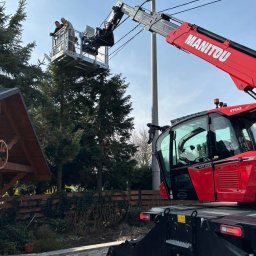 LITBUD Mateusz Litewka - Dwóch pracowników w koszu podnośnika Manitou, pracujących przy linii energetycznej, widoczny fragment dachu altany i drzewa.