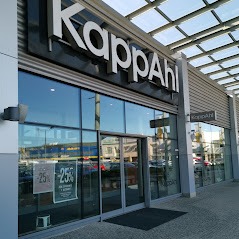 Fasada sklepu KappAhl z dużymi witrynami, widoczne promocje -25% na szybach, jasne oświetlenie dzienne, chodnik przed sklepem, fragment parkingu w tle.