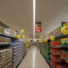 Pusta alejka w supermarkecie w Rumi, udekorowana żółtymi balonami, z perspektywą zbiegającą się w oddali.