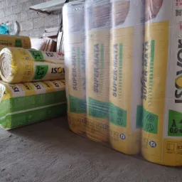 Ułożone rolki wełny mineralnej Isover Super-Mata w żółto-zielonych opakowaniach, zabezpieczone folią, czekają na użycie w magazynie.