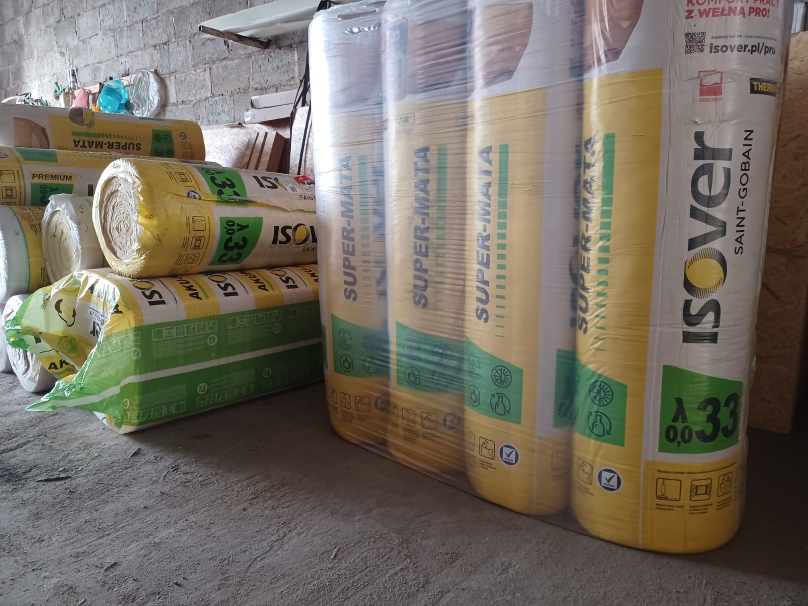 Ułożone rolki wełny mineralnej Isover Super-Mata w żółto-zielonych opakowaniach, zabezpieczone folią, czekają na użycie w magazynie.