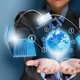 Uśmiechnięta kobieta w garniturze prezentuje w dłoniach hologram globu ziemskiego z połączonymi urządzeniami elektronicznymi, symbolizującymi globalną sieć i komunikację.