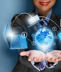 Uśmiechnięta kobieta w garniturze prezentuje w dłoniach hologram globu ziemskiego z połączonymi urządzeniami elektronicznymi, symbolizującymi globalną sieć i komunikację.
