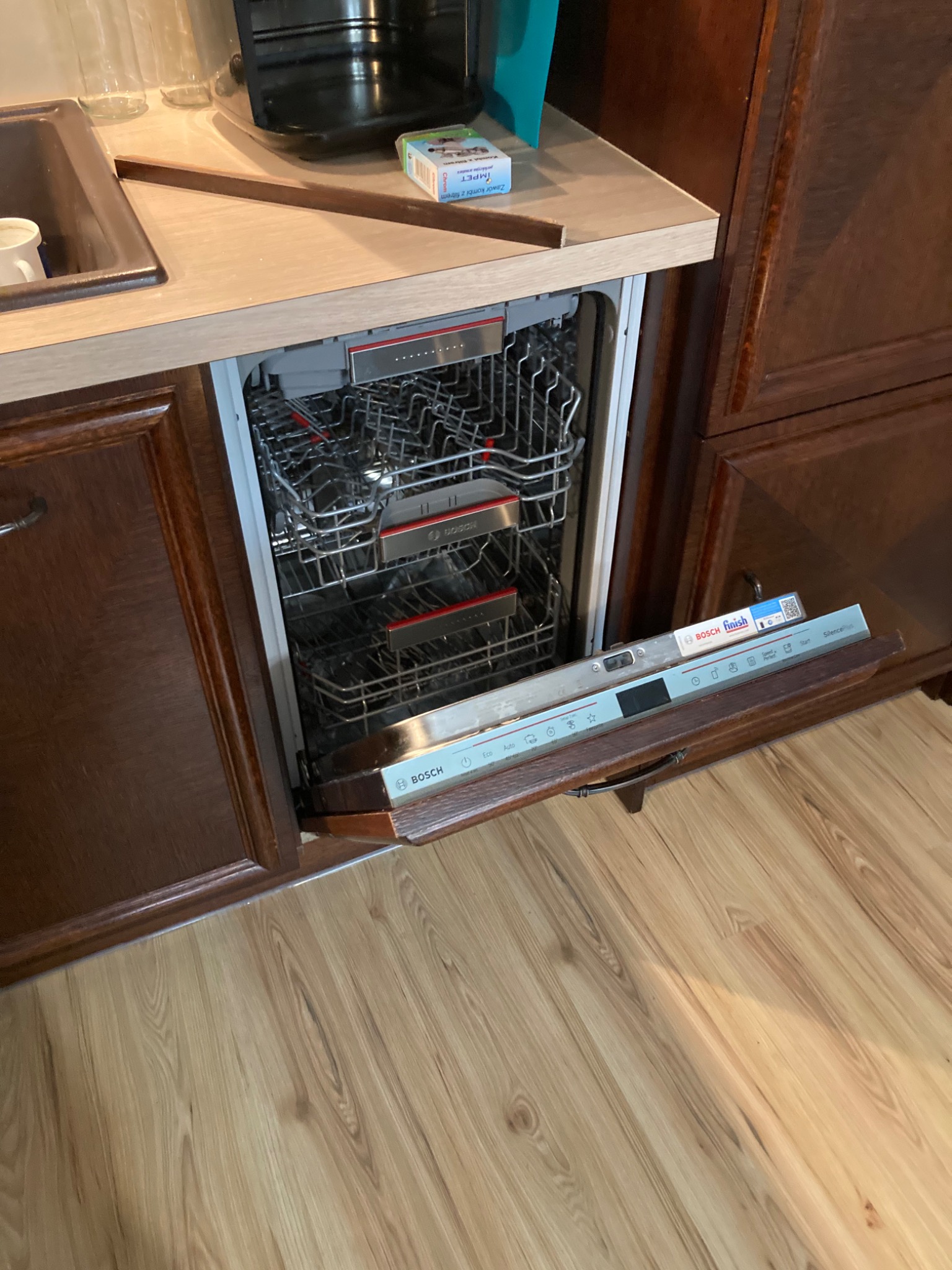 Otwarta zmywarka Bosch w zabudowie kuchennej z ciemnego drewna, widoczny panel sterowania i wnętrze z koszami na naczynia.