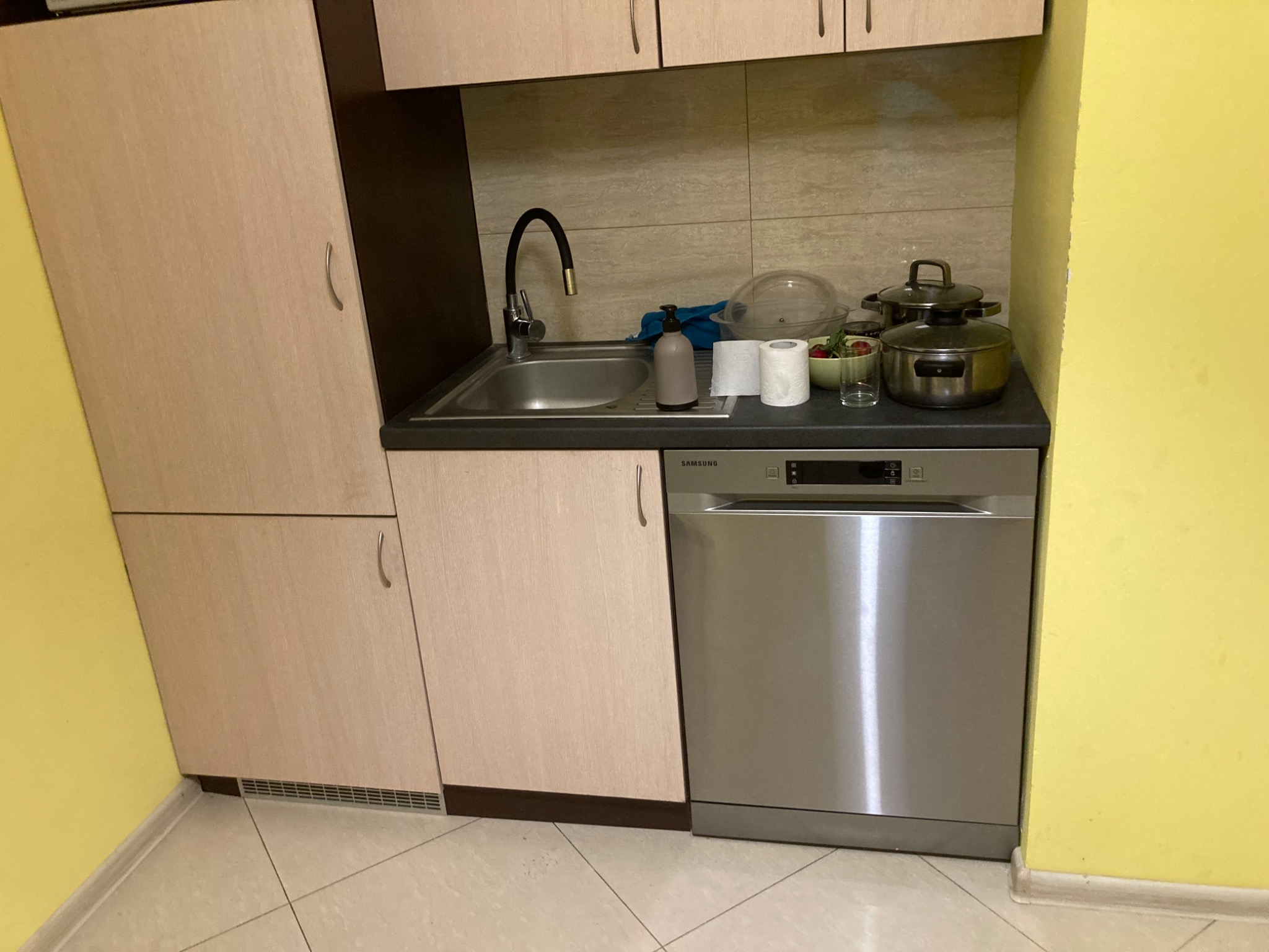 Kuchnia z zabudową, zlewozmywakiem, baterią i zmywarką Samsung, widoczne garnki i akcesoria kuchenne.