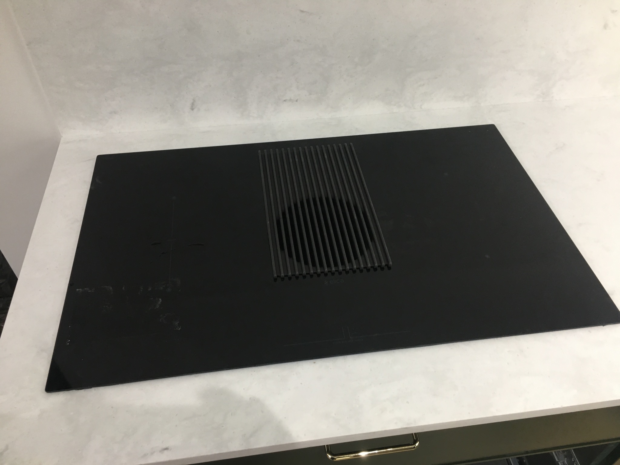 Czarna płyta indukcyjna z wbudowanym okapem marki Elica, zamontowana na białym blacie w Wysogotowie. Widoczne smugi i drobne zabrudzenia na powierzchni płyty.