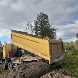 RAFREMS Rafał Cieplak - Żółta wywrotka z podniesioną skrzynią ładunkową, wysypująca ziemię na pryzmę, w tle zieleń i pochmurne niebo.