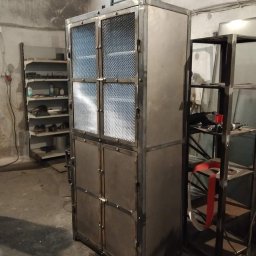 Kuźnia Unikatu Custom Metalwork - Metalowa szafa z siatkowymi drzwiami w warsztacie, widoczne ślady spawania i surowy industrialny styl