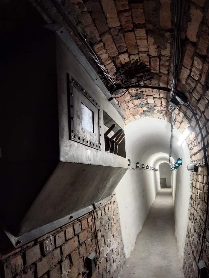 Metalowa konstrukcja z oknami inspekcyjnymi zamontowana w ceglanym tunelu z oświetleniem.