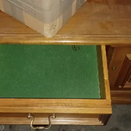 Otwarta szuflada antycznego biurka z zielonym filcem w środku, widoczne rzeźbienia na froncie, na blacie leży kartonowe pudełko.