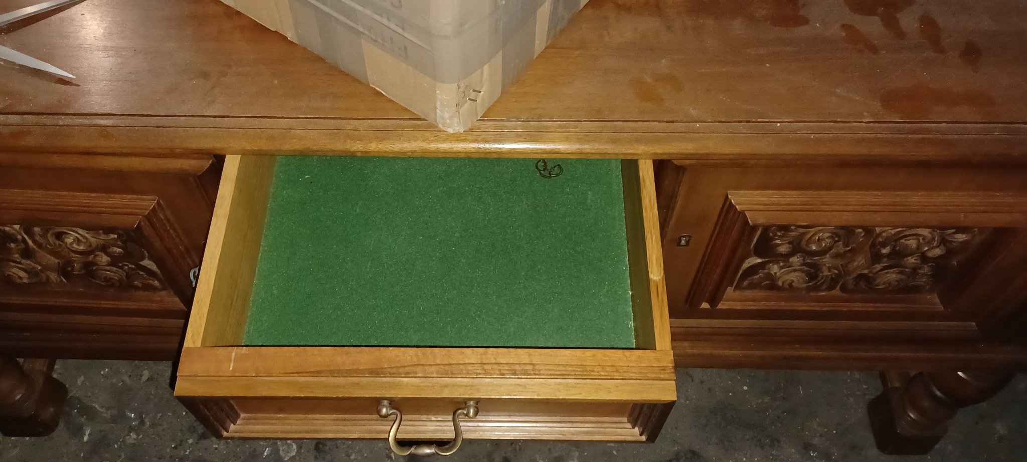 Otwarta szuflada antycznego biurka z zielonym filcem w środku, widoczne rzeźbienia na froncie, na blacie leży kartonowe pudełko.