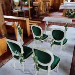 Uroczystość w kościele: Cztery krzesła z zielonym aksamitem i białymi ramami, udekorowane białymi różami i wstążkami, ustawione na białym dywanie wzdłuż nawy głównej.