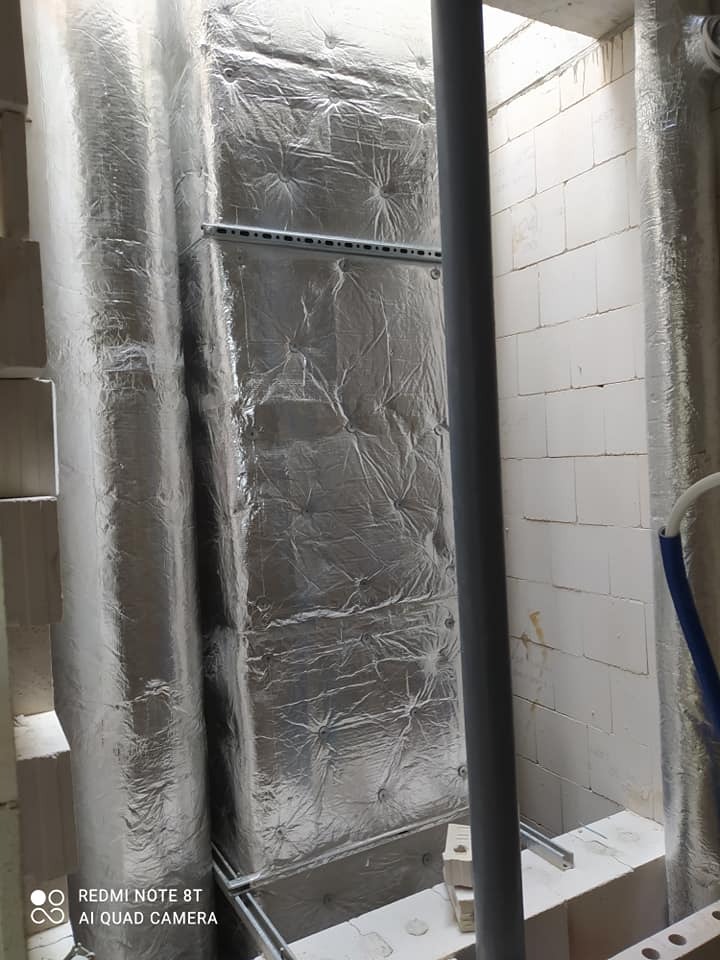 Izolowany kanał wentylacyjny z widocznymi elementami montażowymi, zainstalowany w surowym wnętrzu z białych bloczków.