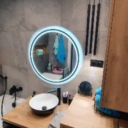 Nowoczesna łazienka z drewnianym blatem, okrągłym lustrem z podświetleniem LED, czarną armaturą i pralką w zabudowie.