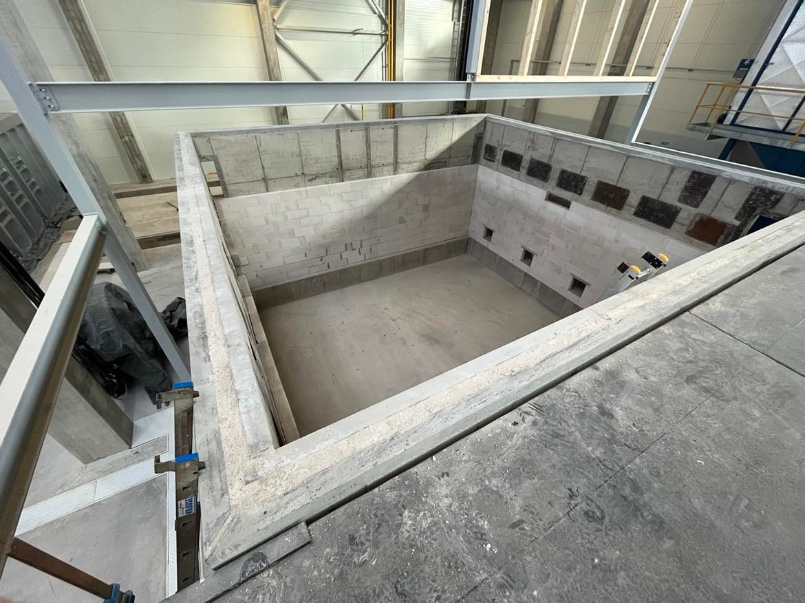 Surowy, betonowy szkielet budynku w trakcie budowy, widok z góry, z widocznymi blokami betonowymi i metalową konstrukcją nośną dachu.